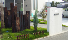 シンプルなコンクリートの門にランダムな枕木を合わせた、シンプルで低コストなスタイル。芝のグリーンが 映えます。